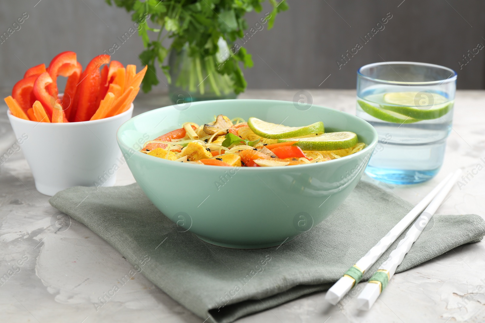 Photo of Stir-fry. Delicious cooked noodles with chicken and vegetables in bowl served on gray textured table