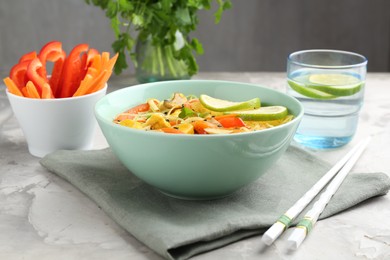 Photo of Stir-fry. Delicious cooked noodles with chicken and vegetables in bowl served on gray textured table