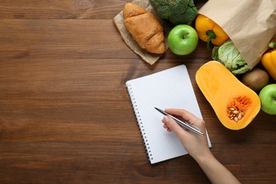 Photo of Woman calculating calories at wooden table with food products, top view and space for text. Weight loss concept