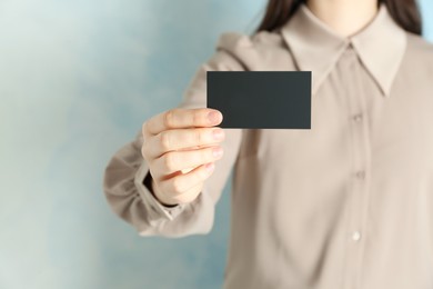 Woman holding blank business card on light blue background, closeup. Mockup for design