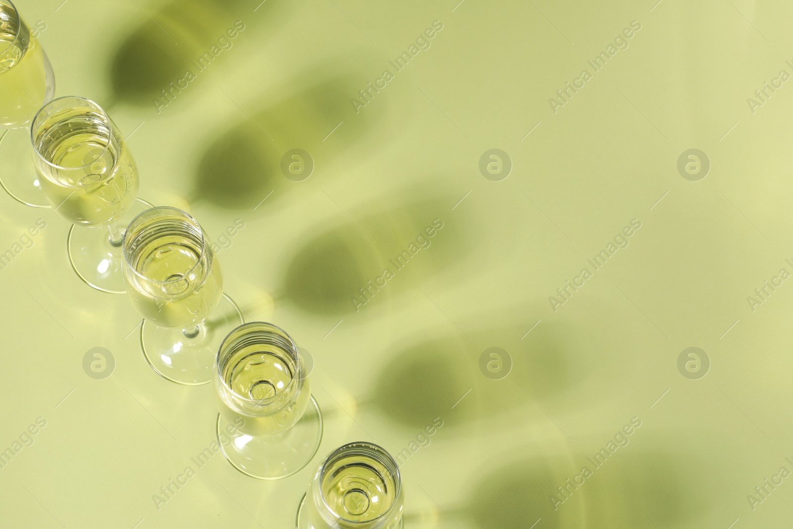 Photo of Glasses of delicious sparkling wine on light yellow background, above view. Space for text