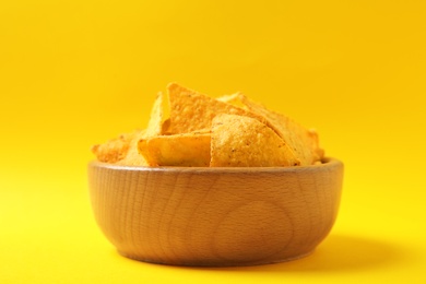 Photo of Tasty mexican nachos chips in wooden bowl on yellow background