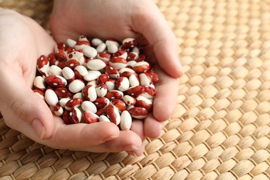 Photo of Woman holding pile of beans over wicker table, closeup. Vegetable seeds planting