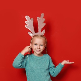 Cute little girl with reindeer antlers prop on red background. Christmas celebration