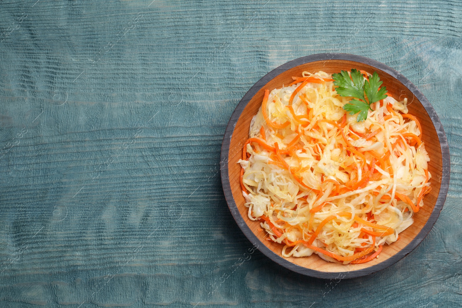 Photo of Tasty fermented cabbage with carrot on blue wooden table, top view. Space for text