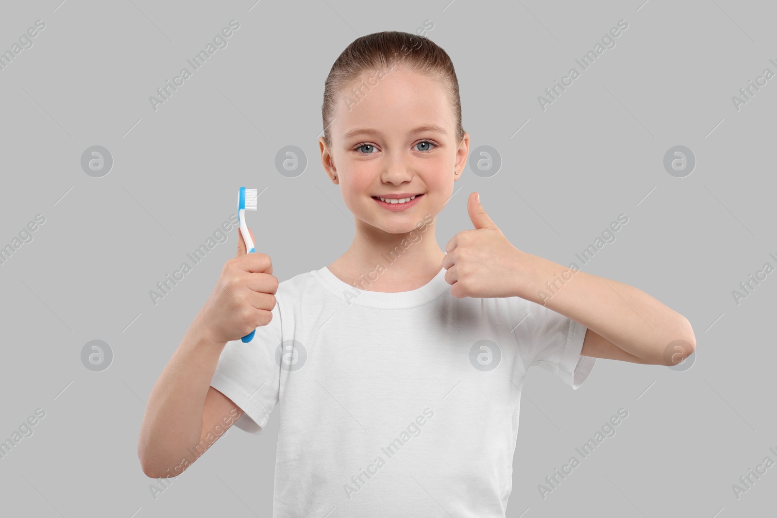 Photo of Happy girl holding toothbrush and showing thumb up on light grey background