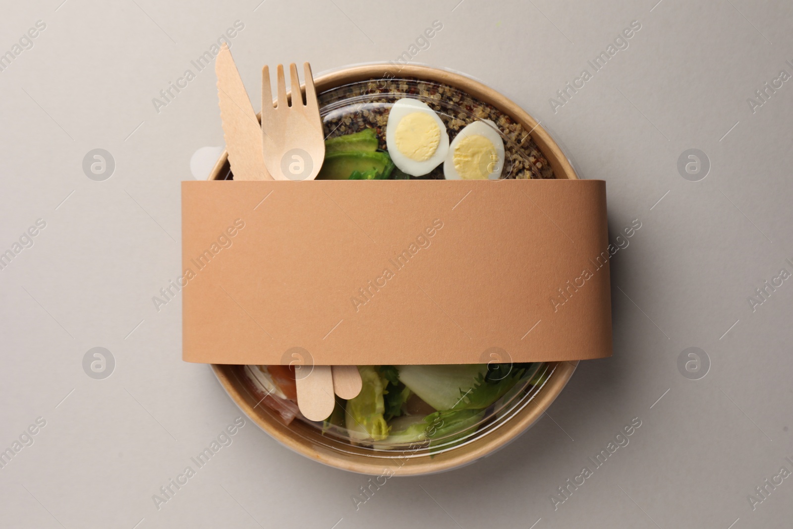 Photo of Tasty food in container with wooden fork and knife on light background, top view. Space for text