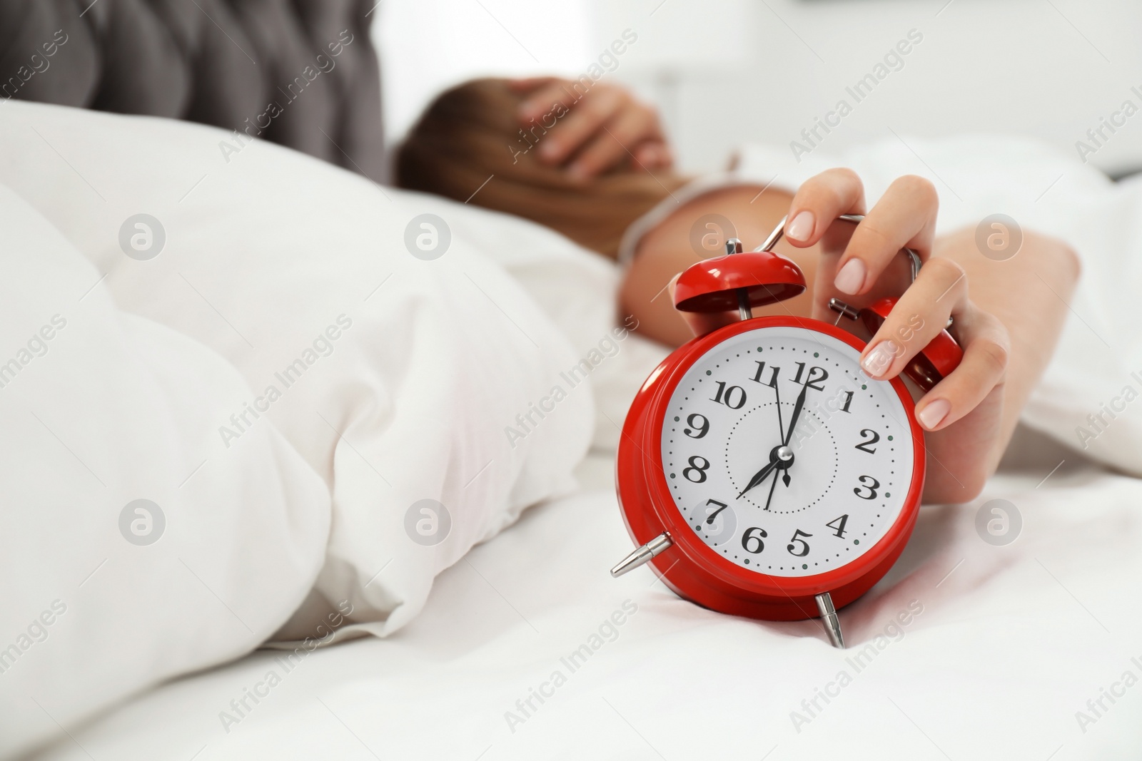 Photo of Woman turning off alarm clock in bedroom