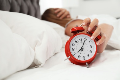 Photo of Woman turning off alarm clock in bedroom