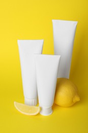 Photo of Blank tubes of toothpaste and fresh lemon on yellow background