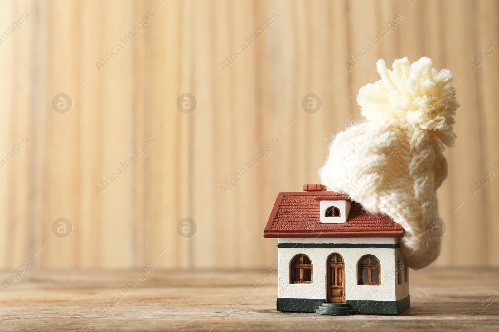 Photo of Wooden house model and hat on wooden table, space for text. Heating efficiency