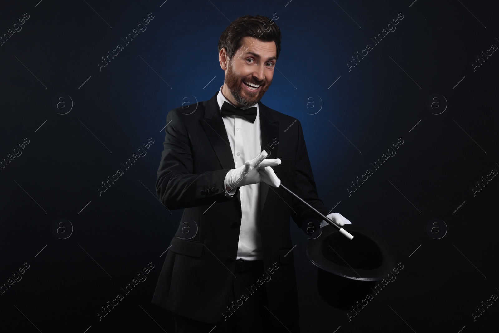 Photo of Happy magician showing magic trick with top hat on dark blue background