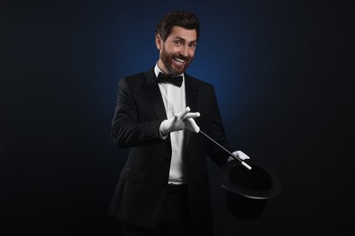 Happy magician showing magic trick with top hat on dark blue background