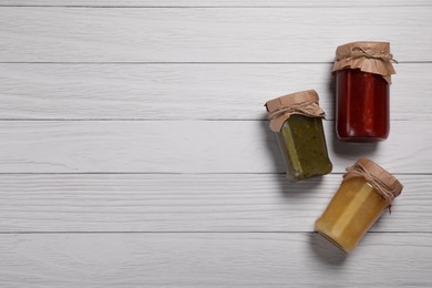 Jars with preserved fruit jams on white wooden table, flat lay. Space for text