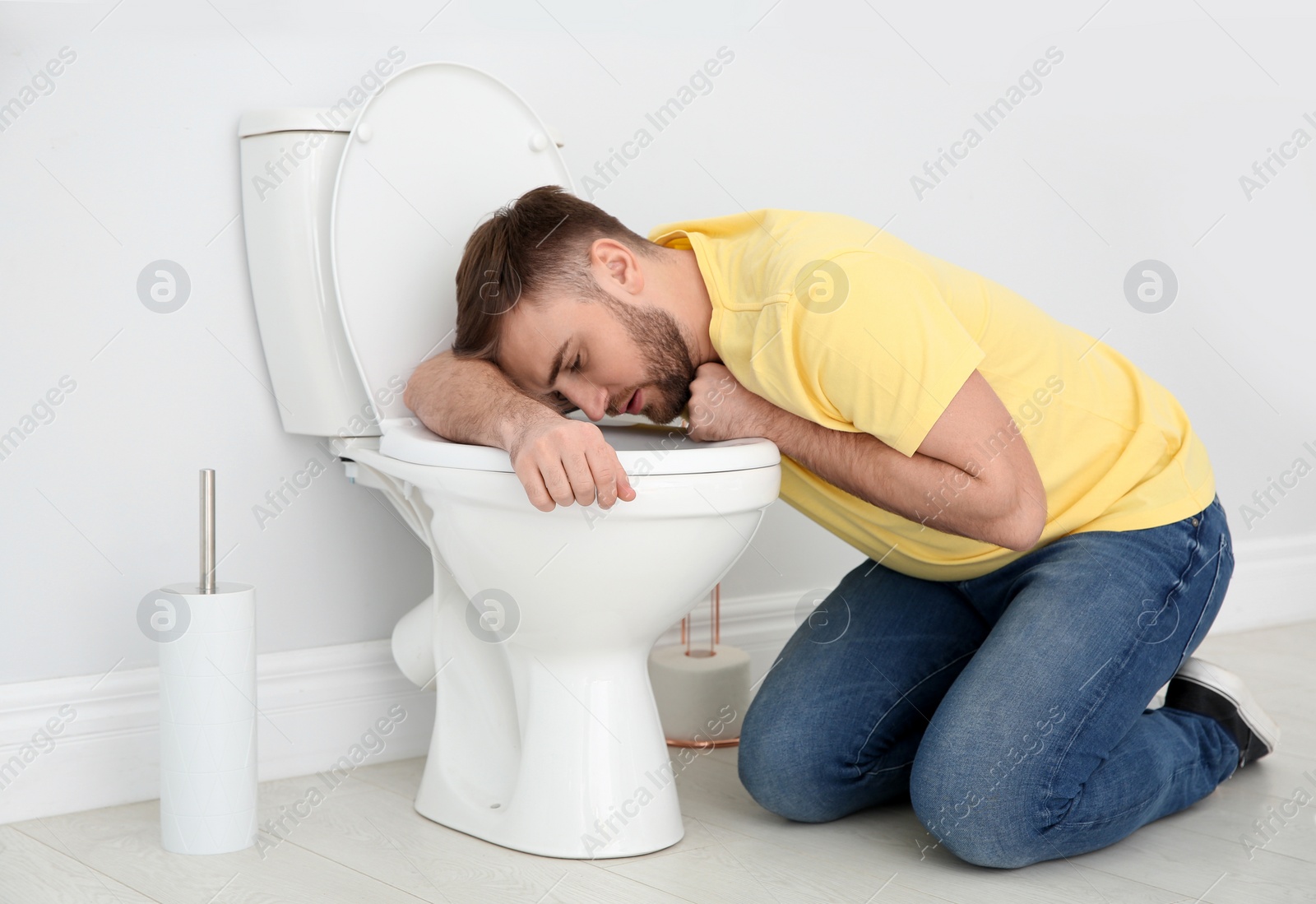 Photo of Young man suffering from nausea over toilet bowl indoors