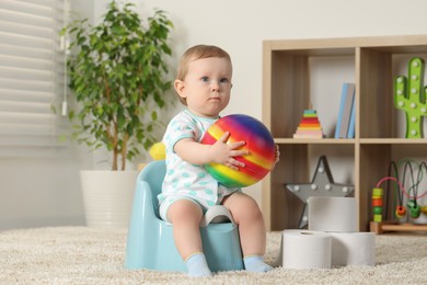 Photo of Little child with ball sitting on plastic baby potty indoors