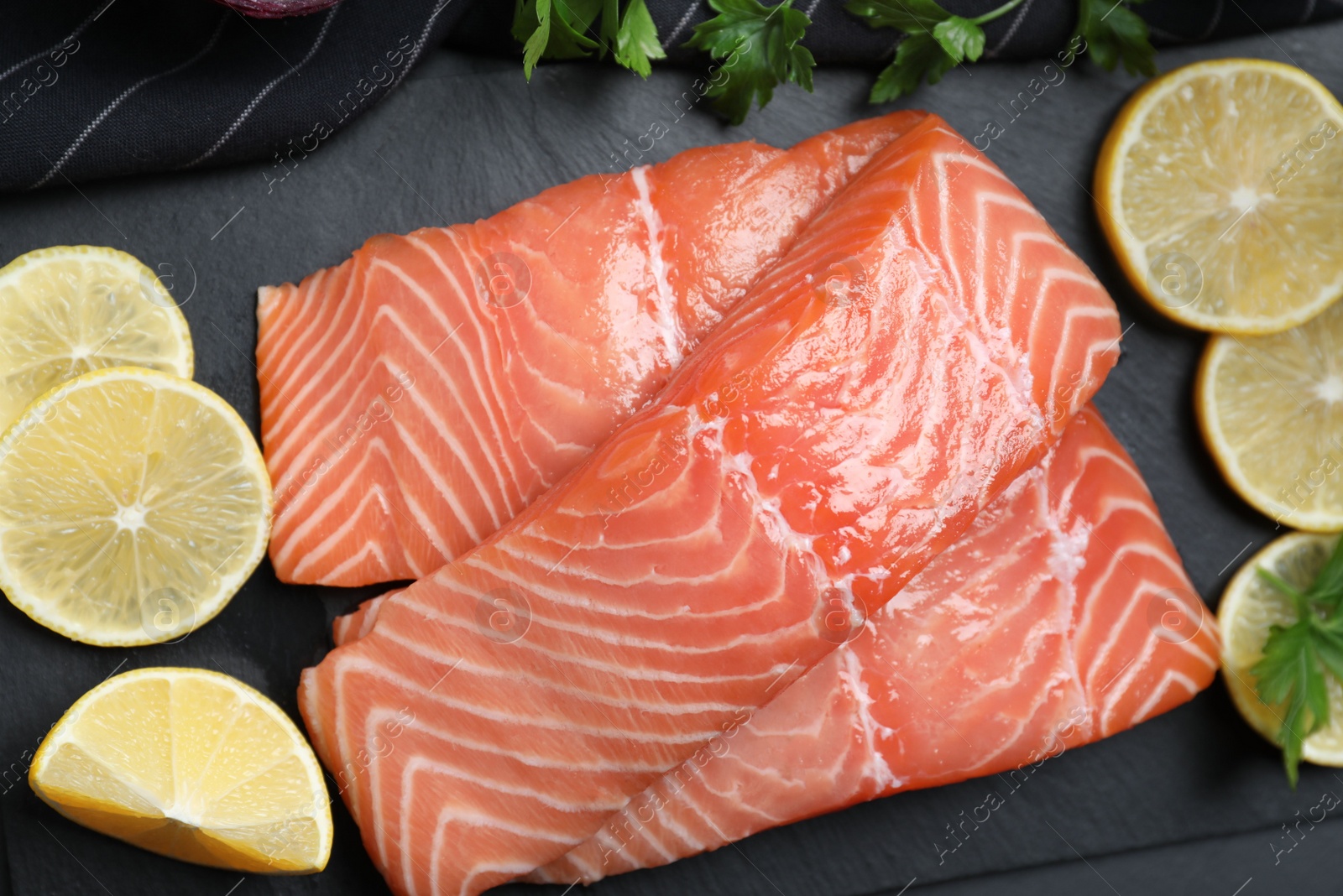 Photo of Top view of fresh raw salmon with lemon and parsley on slate plate. Fish delicacy