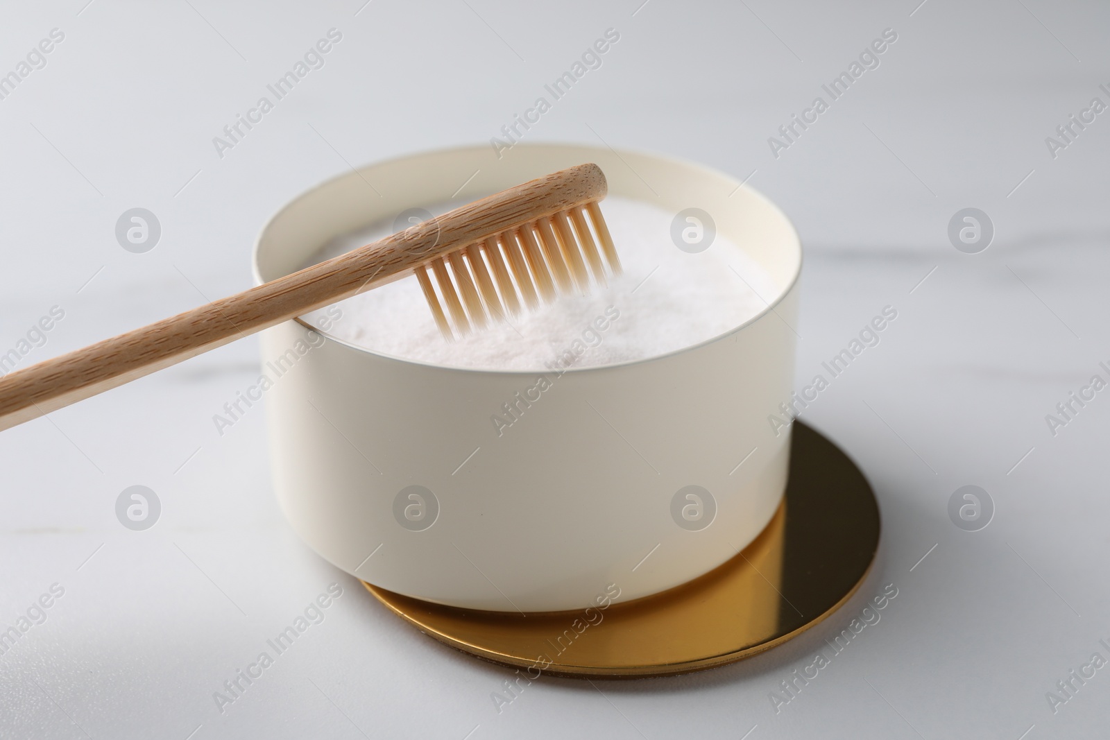 Photo of Bamboo toothbrush and bowl of baking soda on white table, closeup