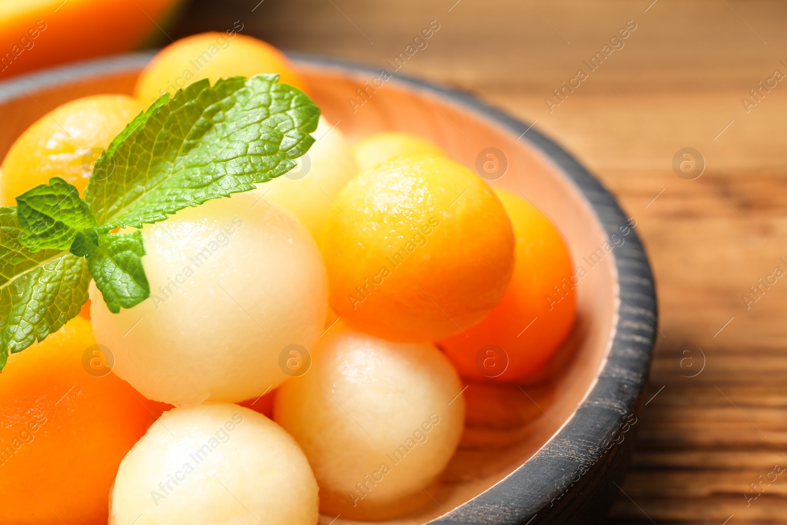 Photo of Different melon balls with mint on wooden plate, closeup