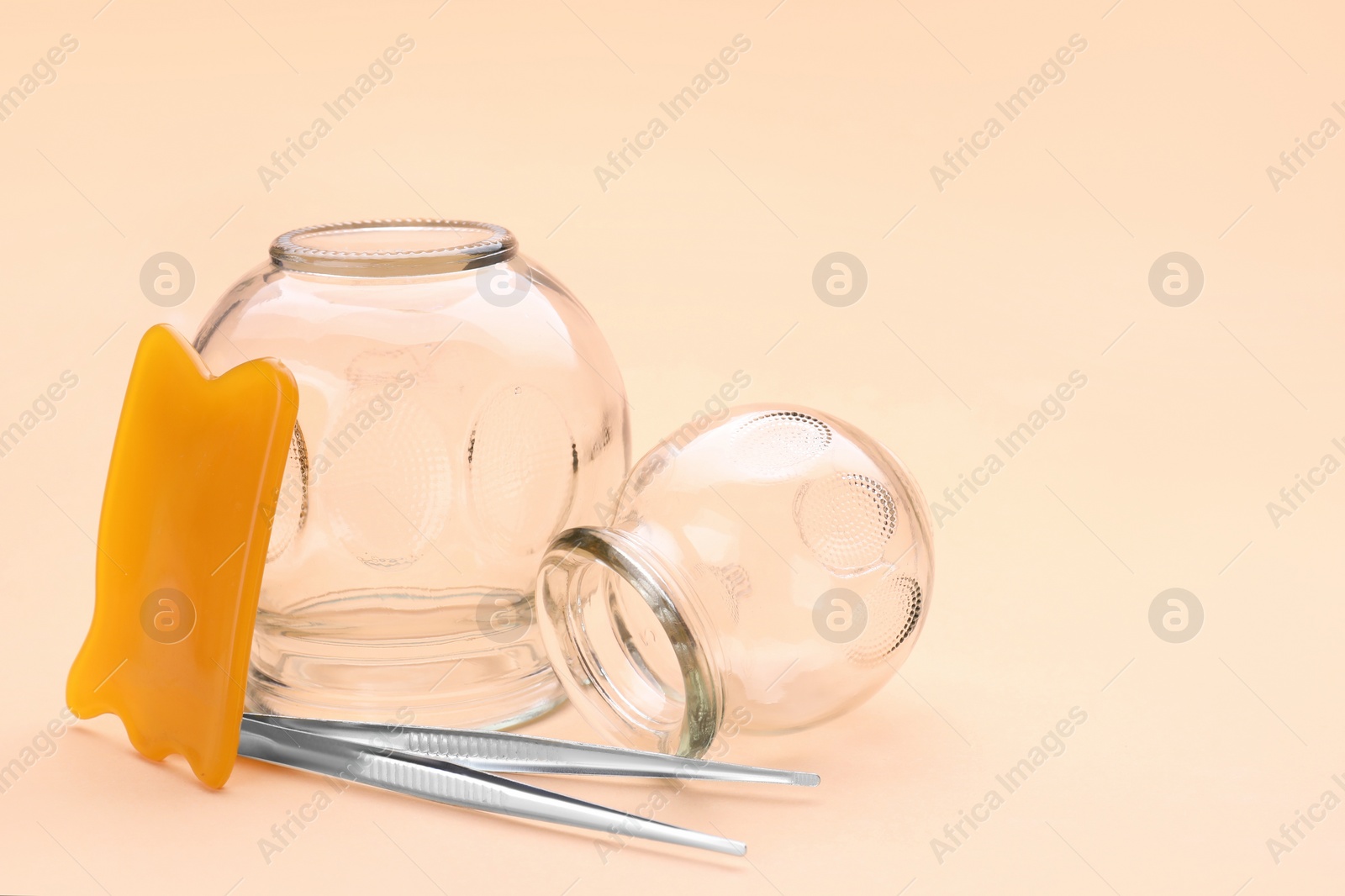 Photo of Glass cups, gua sha and tweezers on light coral background, closeup with space for text. Cupping therapy