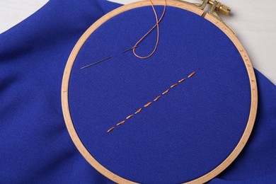 Blue cloth with stitches, sewing thread and needle on table, top view