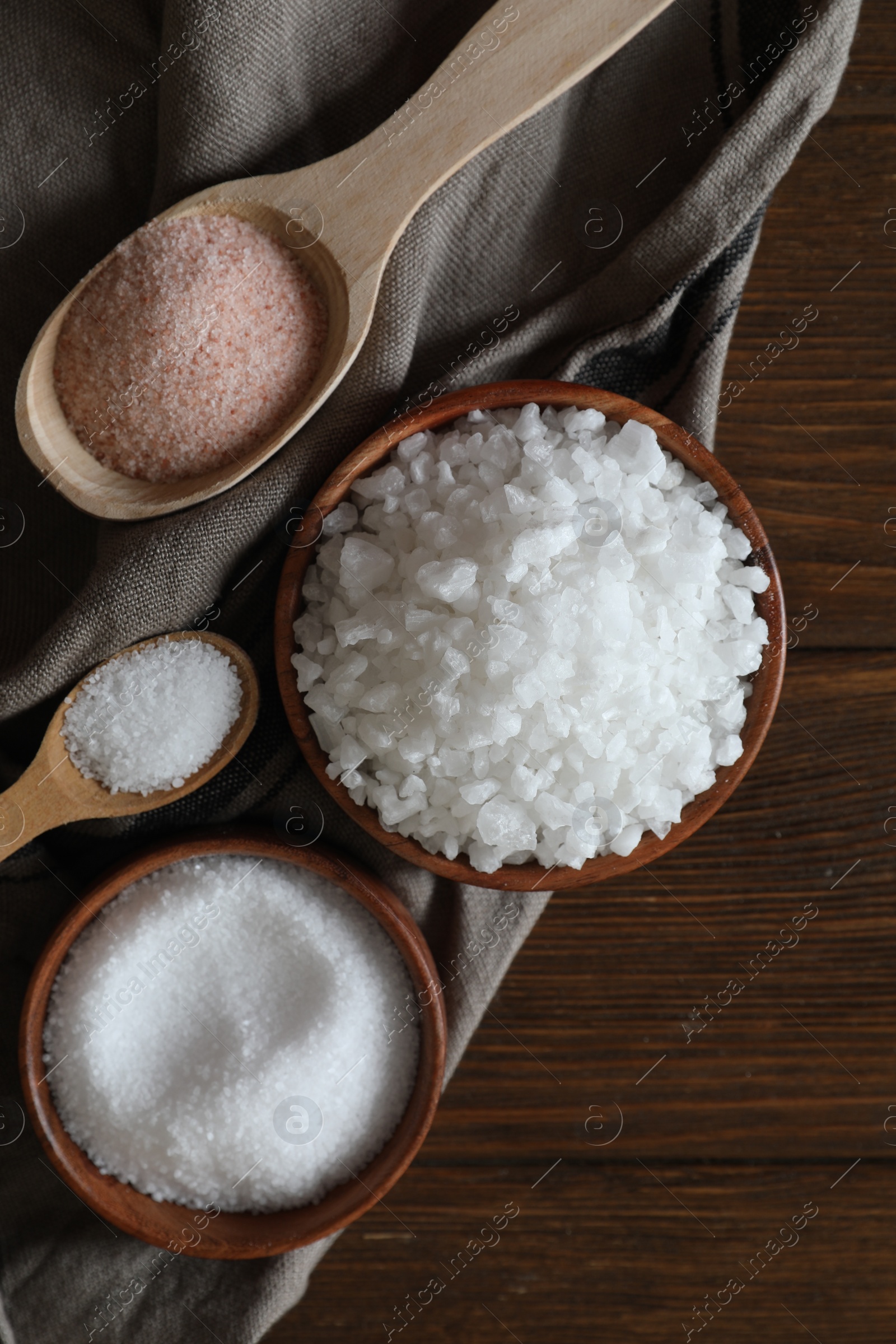 Photo of Different types of organic salt on wooden table, flat lay