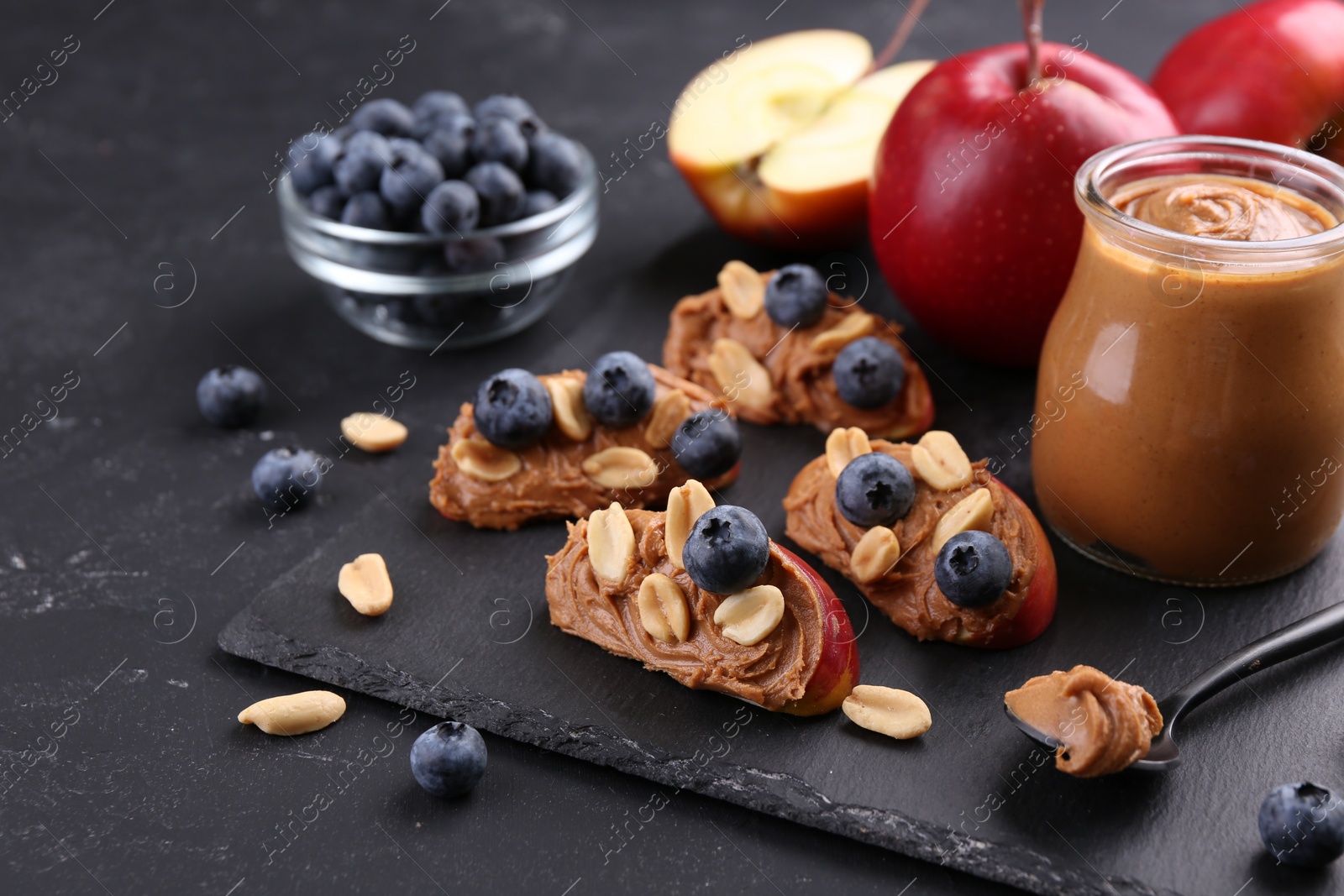 Photo of Fresh apples with peanut butter and blueberries on dark table