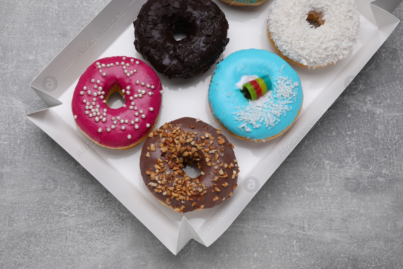 Photo of Box with different tasty glazed donuts on light grey table, top view