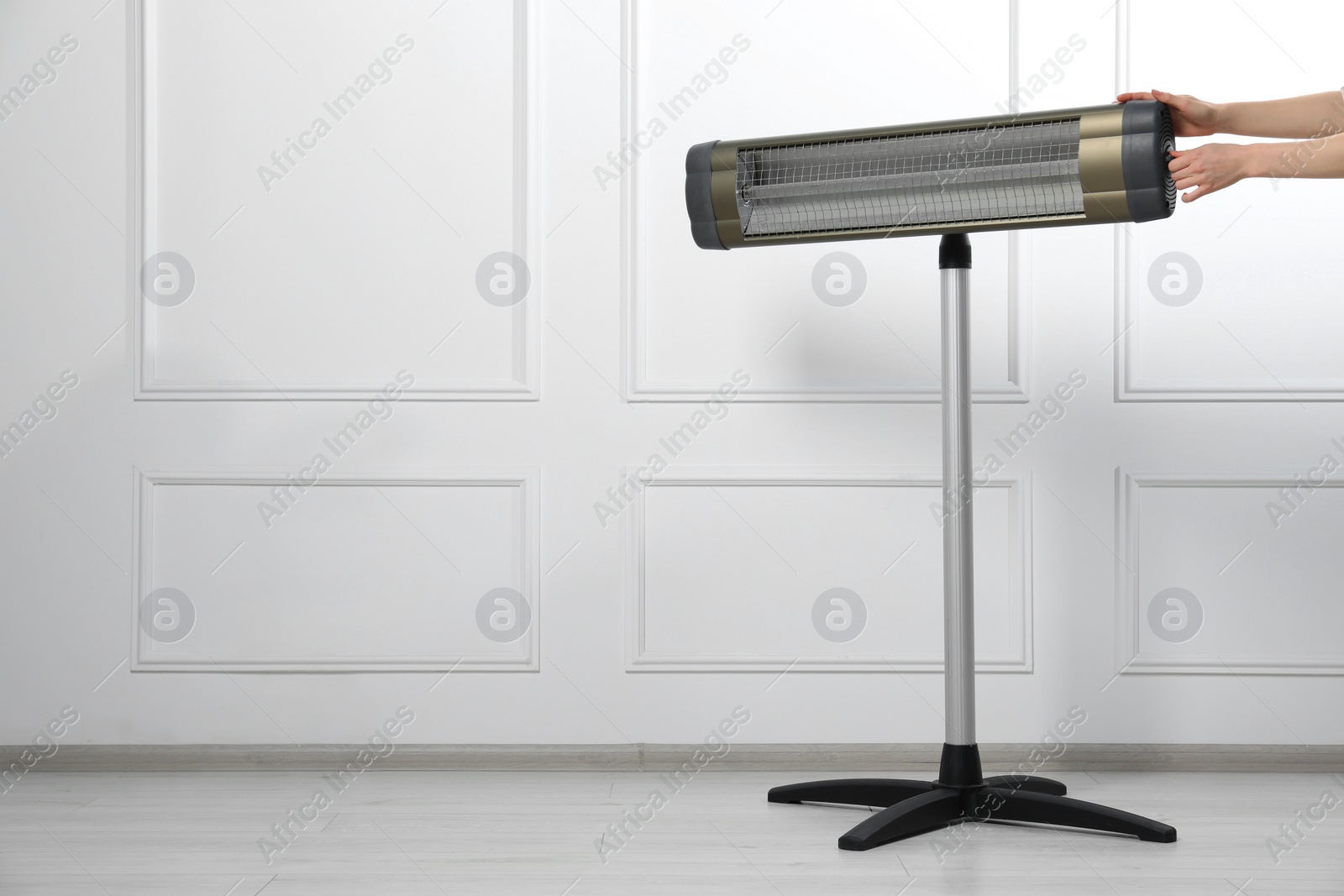 Photo of Young woman adjusting temperature on modern electric infrared heater near white wall, closeup. Space for text
