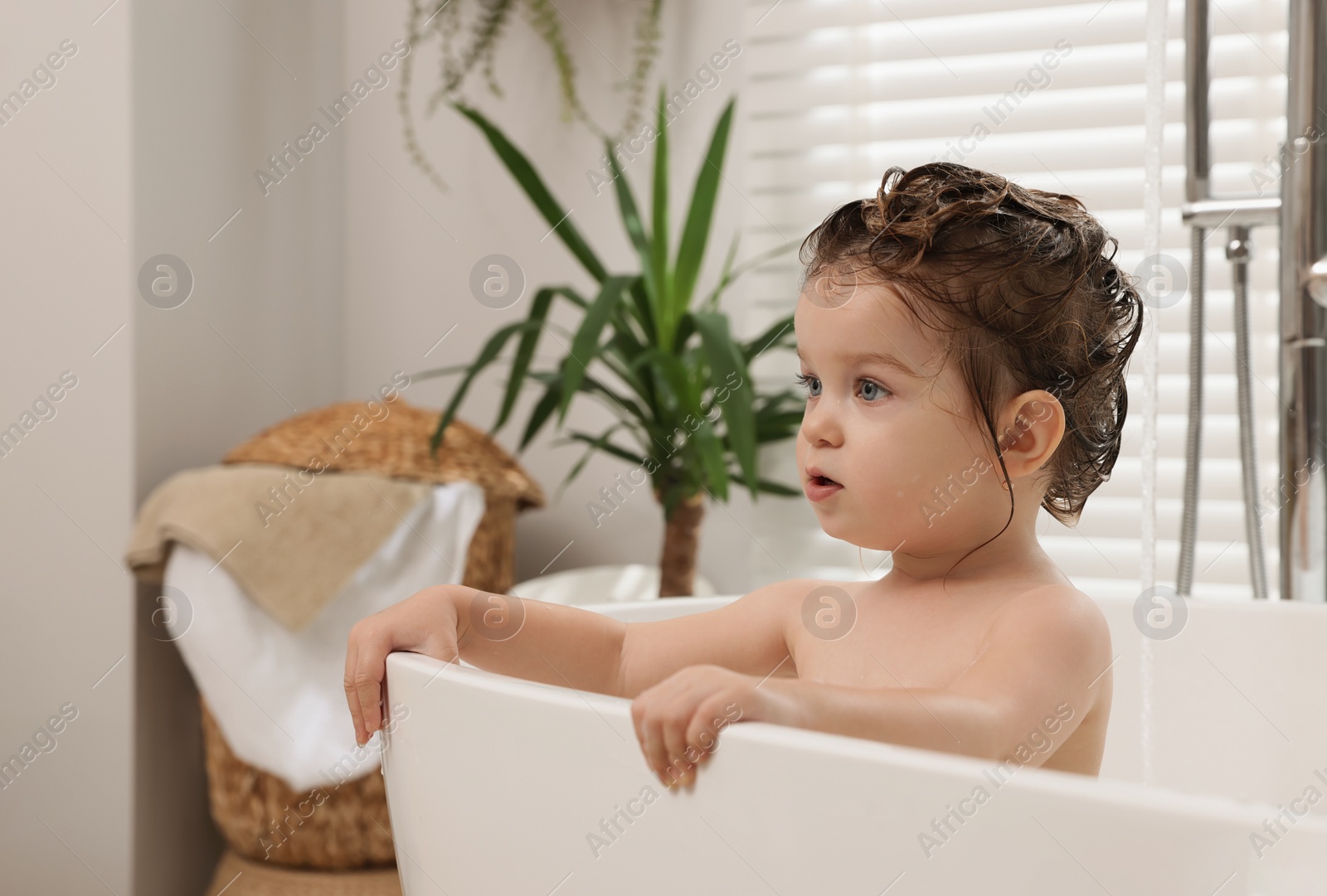 Photo of Cute little girl washing hair with shampoo in bathroom