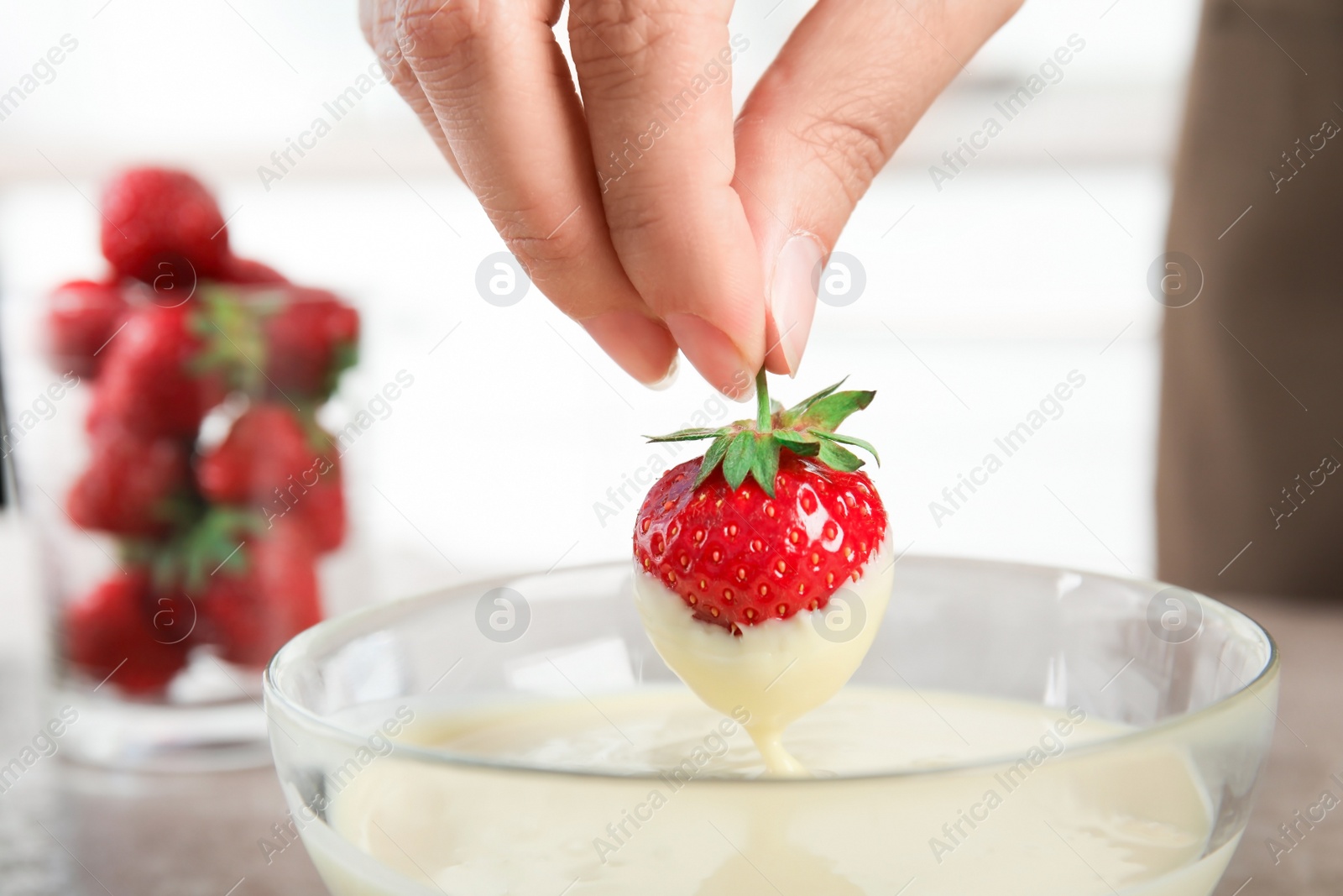 Photo of Woman dipping ripe strawberry into bowl with white melted chocolate, closeup