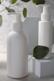 Different face cleansing products and eucalyptus leaves on light grey table