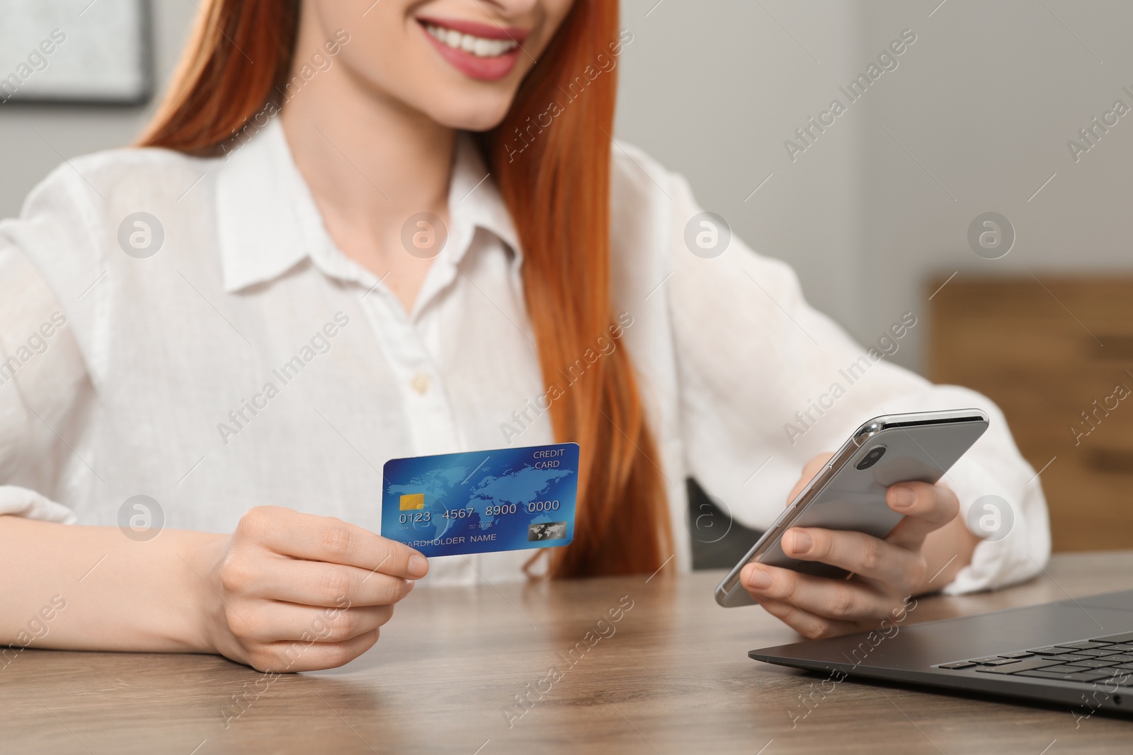 Photo of Woman with credit card using smartphone for online shopping at wooden table indoors, closeup