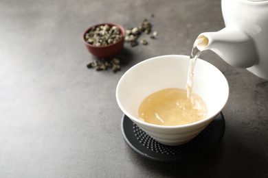 Photo of Pouring green tea into cup on grey table. Space for text