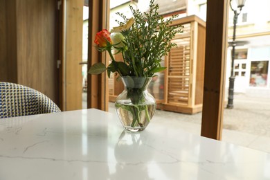 Photo of Bouquet of beautiful flowers in glass vase on table at cafeteria