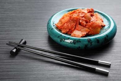 Photo of Plate of spicy cabbage kimchi and chopsticks on black wooden table
