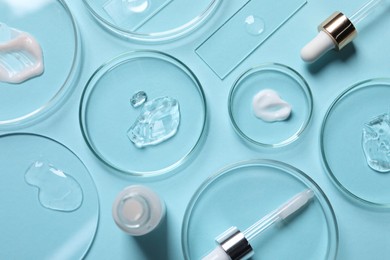 Photo of Petri dishes with samples of cosmetic serums, bottle and pipettes on light blue background, flat lay