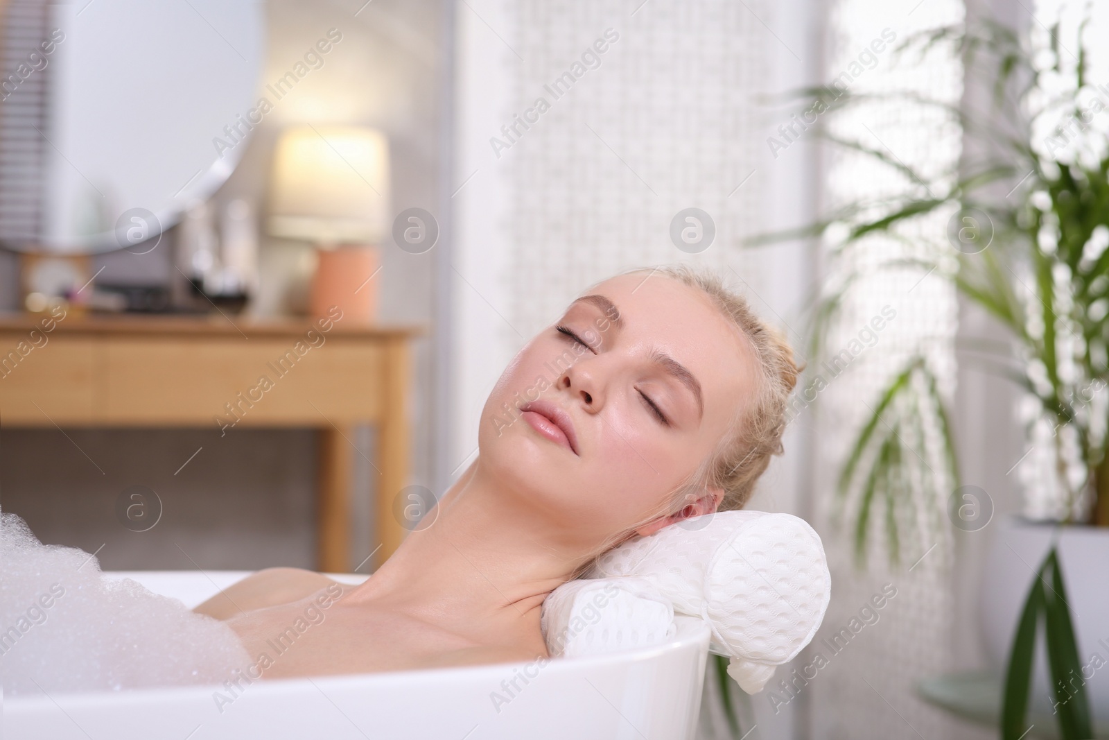 Photo of Young woman using pillow while enjoying bubble bath indoors