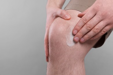 Photo of Man applying ointment onto his knee on light grey background, closeup. Space for text