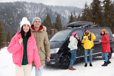 Happy couple and their friends near car on snowy road. Winter vacation