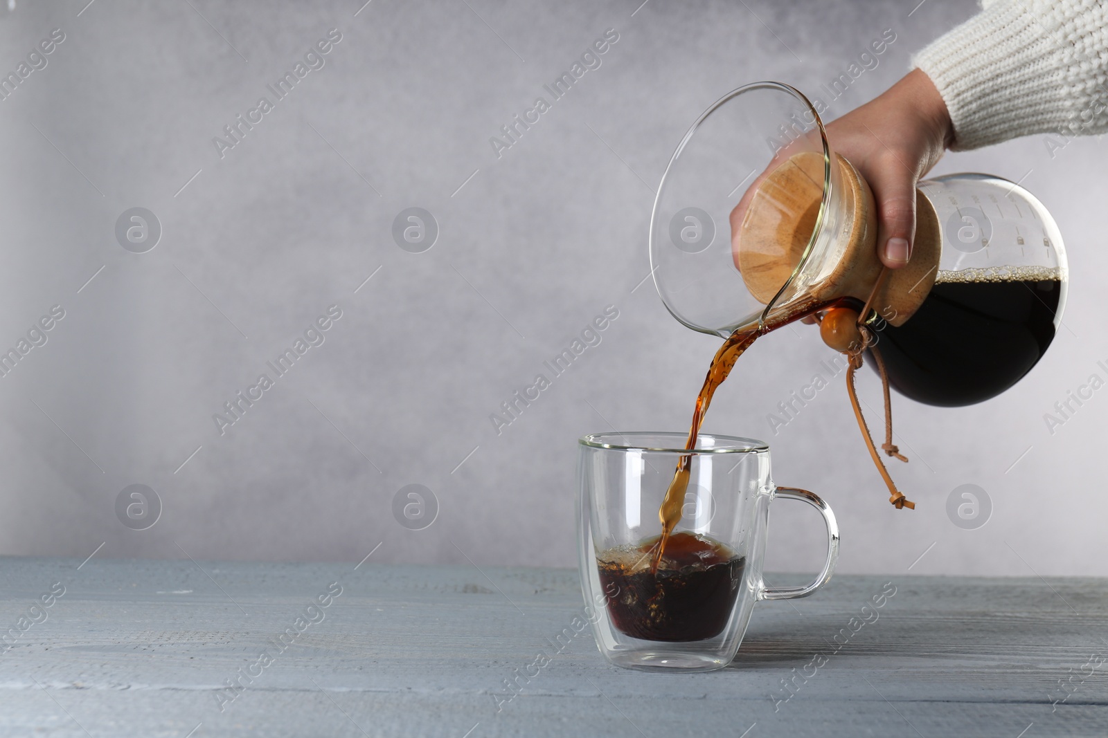 Photo of Woman pouring tasty drip coffee into cup at grey wooden table, closeup. Space for text