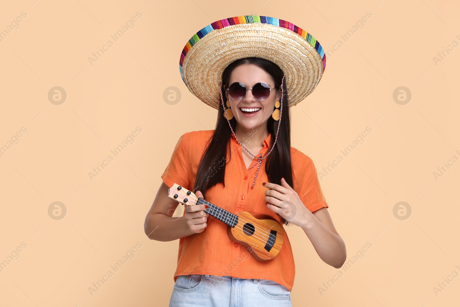 Photo of Young woman in Mexican sombrero hat playing ukulele on beige background