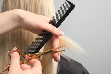 Photo of Hairdresser cutting client's hair with scissors on light grey background, closeup. Space for text