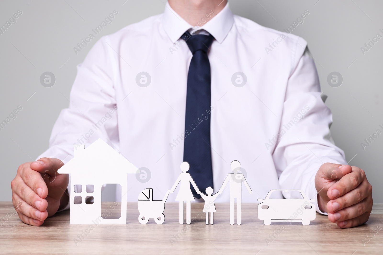 Photo of Man protecting figures of family, car and house at wooden table. closeup. Insurance concept