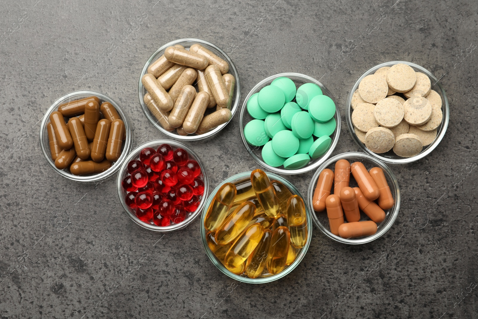 Photo of Different dietary supplements in glass bowls on grey table, flat lay