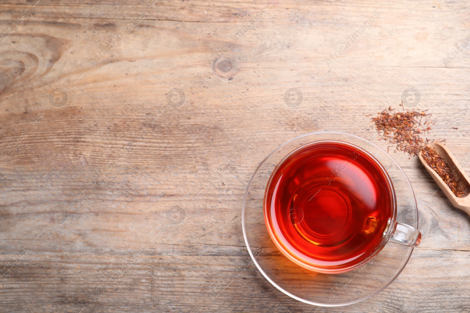 Photo of Freshly brewed rooibos tea and dry leaves on wooden table, flat lay. Space for text