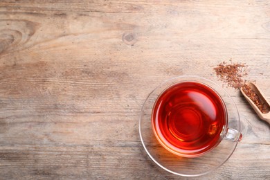 Photo of Freshly brewed rooibos tea and dry leaves on wooden table, flat lay. Space for text