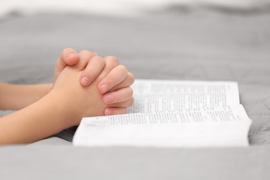 Photo of Girl holding hands clasped while praying over Bible indoors, closeup