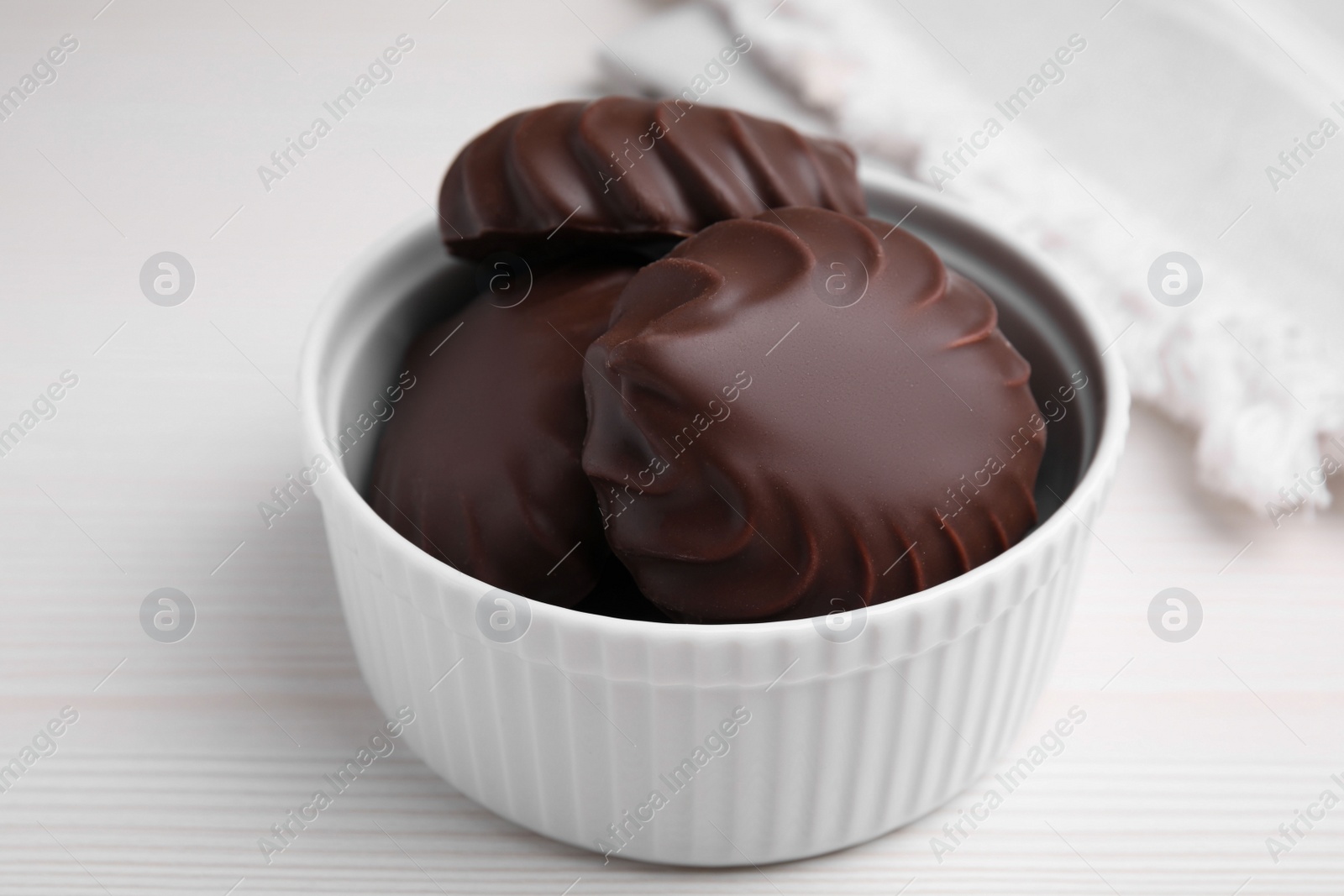 Photo of Delicious chocolate covered zephyrs in bowl on white wooden table, closeup