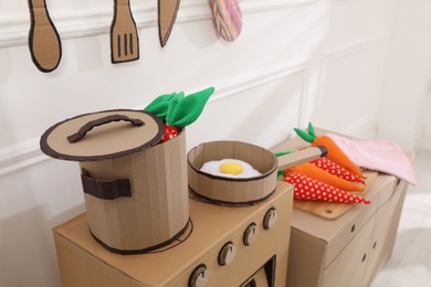 Photo of Toy cardboard kitchen with stove and utensils indoors